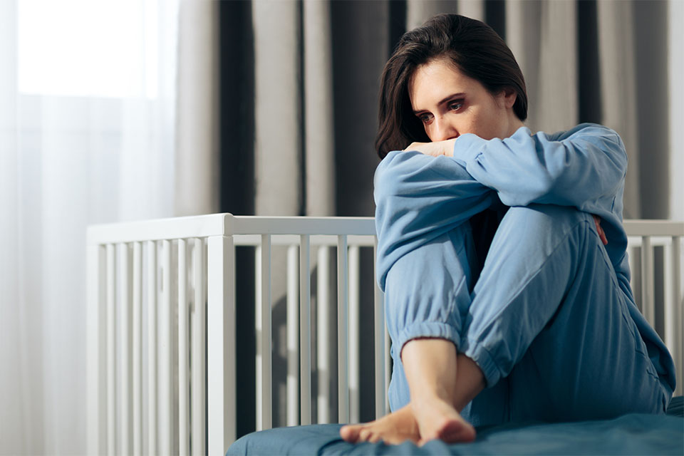 woman with postpartum depression by a crib